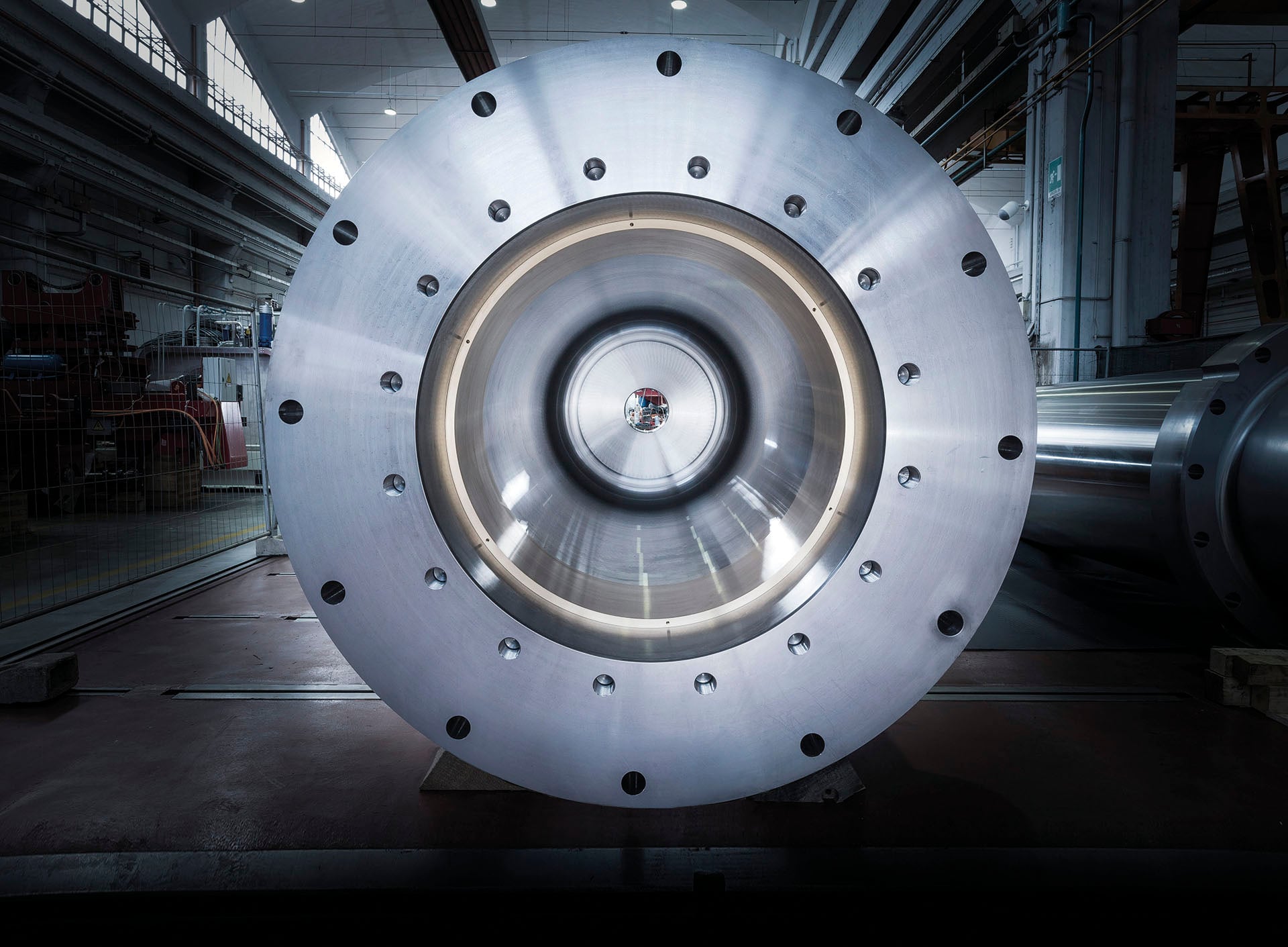 Large steel cylinder end cover with a ring of bolts in an industrial hall